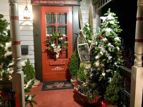 A festive porch decorated for Christmas with a red door, wreaths, and greenery. Snowy accents add a cozy touch.