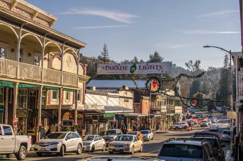 A charming street scene with shops and cars, decorated for the Parade of Lights in a festive, small-town atmosphere.