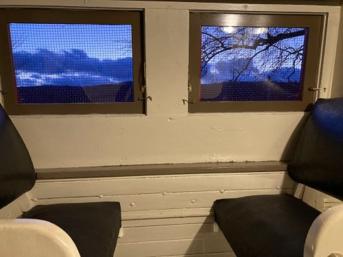Interior view of a small room with two windows showing a twilight sky and bare tree branches outside.
