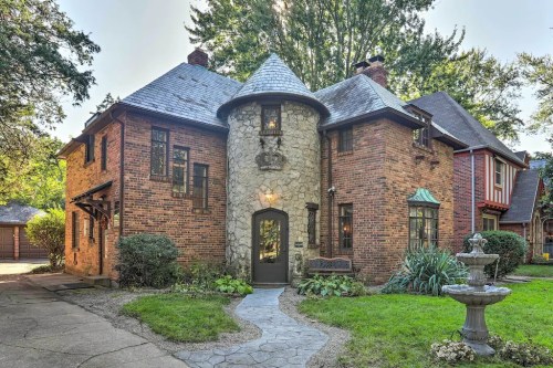 Charming brick house with a stone turret, surrounded by greenery and a pathway leading to the entrance.