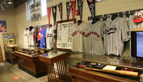 Display of vintage baseball jerseys and memorabilia in a museum setting, featuring various team logos and artifacts.