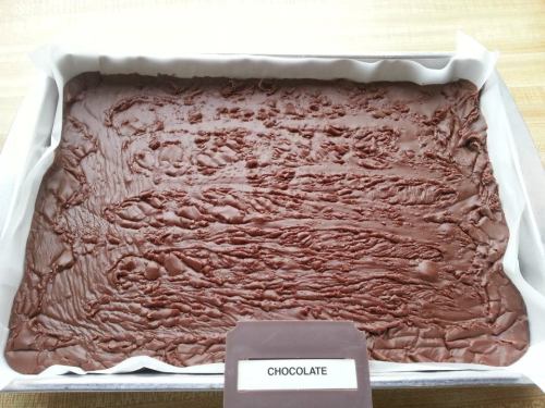 A rectangular tray filled with smooth, melted chocolate, labeled "CHOCOLATE" at the bottom.