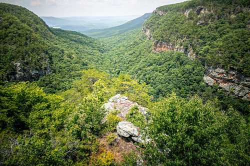 A lush green valley surrounded by mountains, with a rocky outcrop in the foreground under a cloudy sky.