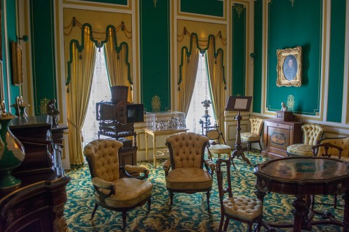 A vintage room with green walls, ornate curtains, antique furniture, and decorative accents, creating a classic atmosphere.
