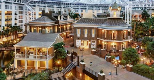 A beautifully designed indoor atrium featuring buildings, greenery, and a serene waterway.