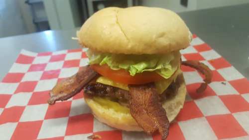 A delicious burger with lettuce, tomato, cheese, and crispy bacon on a toasted bun, served on a red and white checkered paper.
