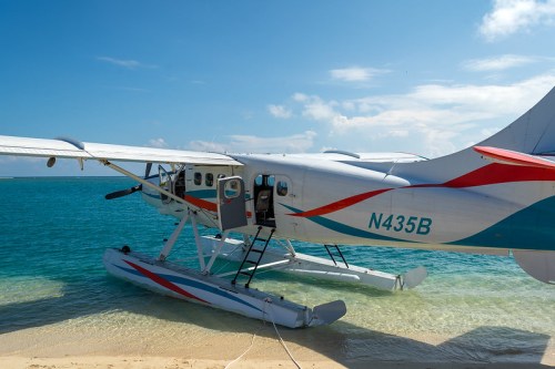 A seaplane parked on a sandy beach with turquoise water and a clear blue sky in the background.