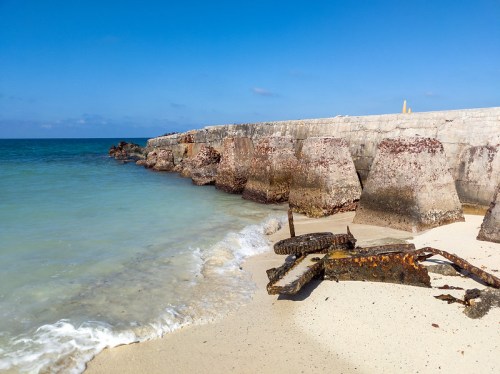 A sandy beach with a rocky jetty extending into calm blue waters under a clear sky.