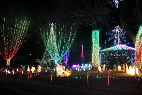 Colorful holiday lights illuminate trees and decorations in a festive outdoor display, featuring a gazebo and candy canes.