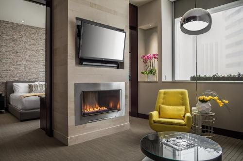 A modern hotel room featuring a yellow chair, fireplace, TV, and large windows with plants and flowers.