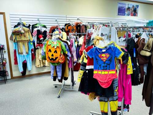 A variety of colorful costumes and Halloween outfits displayed on racks in a store.