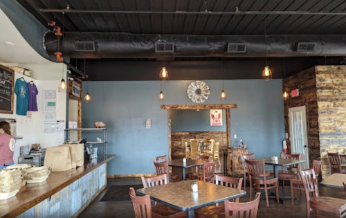 Cozy restaurant interior with wooden decor, tables, and a clock on the wall. A staff member is seen in the background.