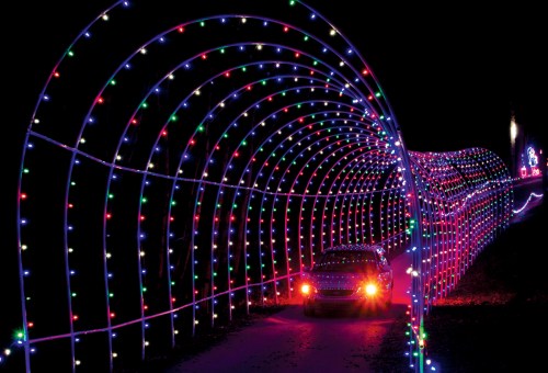 A car drives through a colorful, illuminated tunnel of lights in a dark setting.