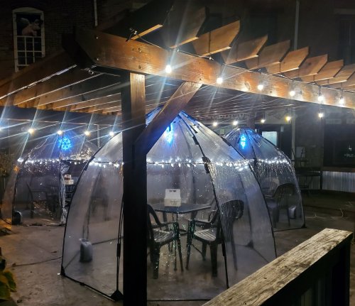 Outdoor dining area with clear domes, string lights, and a wooden pergola, creating a cozy atmosphere at night.