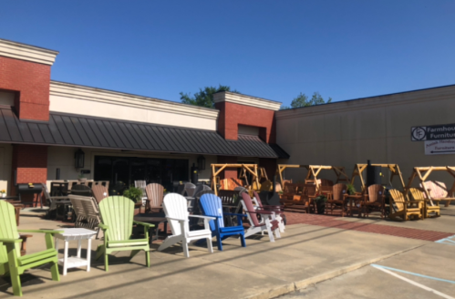 Outdoor display of colorful Adirondack chairs and swings in front of a furniture store on a sunny day.