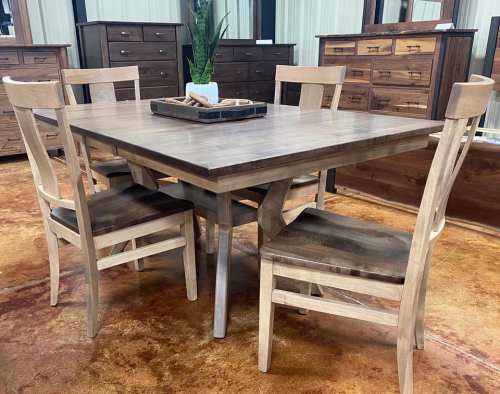 A wooden dining table with four chairs, set in a furniture showroom with various wooden cabinets in the background.