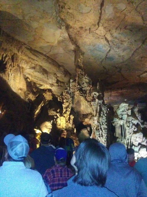 A group of people stands in a cave, admiring impressive rock formations illuminated by soft lighting.