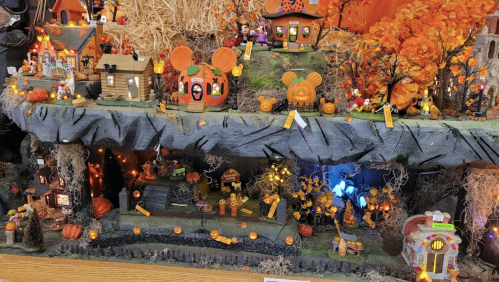 A colorful Halloween display featuring miniature houses, pumpkins, and festive decorations with lights and autumn foliage.