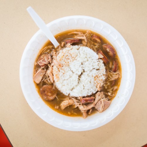 A bowl of savory stew with shredded chicken, sausage, and a mound of white rice in the center.