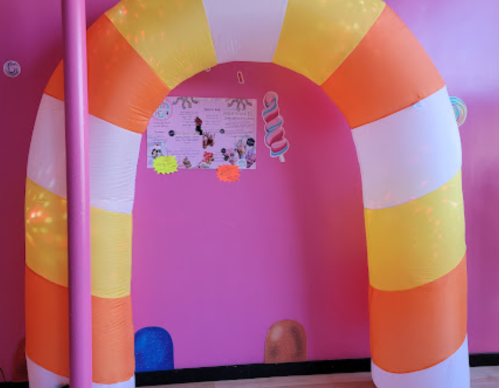 An inflatable candy corn archway in front of a pink wall with colorful decorations.