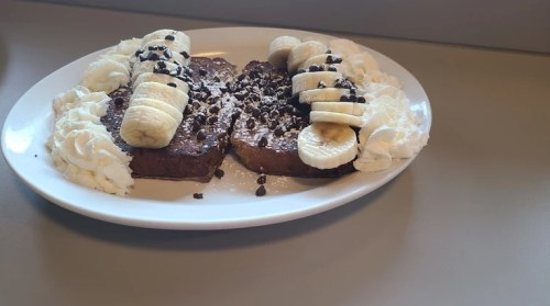 A plate of French toast topped with banana slices, chocolate chips, and whipped cream.