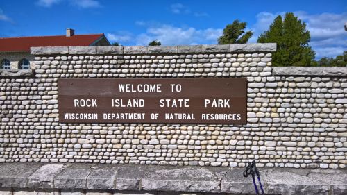 Sign welcoming visitors to Rock Island State Park, featuring stone wall and blue sky in the background.