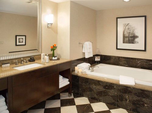 A modern bathroom featuring a marble tub, sink area, and decorative artwork, with neatly arranged towels and a flower vase.