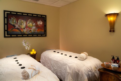 A serene spa room with two massage tables, candles, and a floral painting on the wall, creating a calming atmosphere.