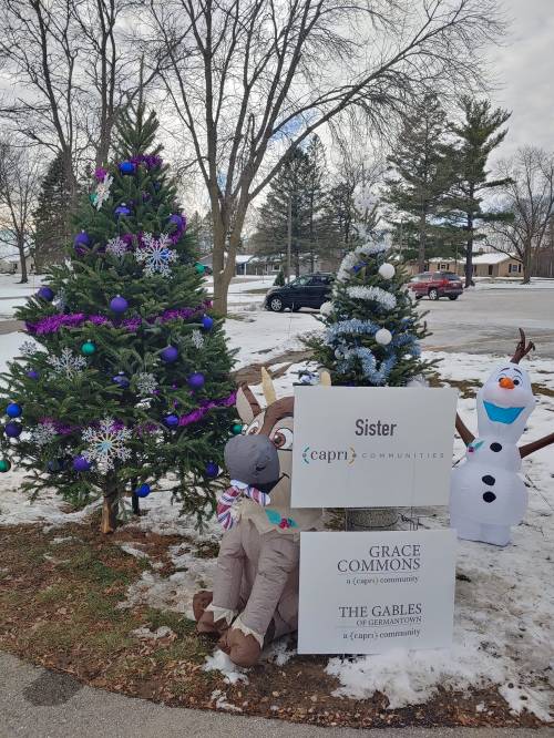 Two decorated Christmas trees with a sign for Grace Commons, featuring a reindeer and a snowman nearby.