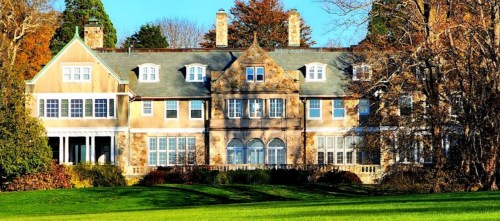 A large, elegant mansion with stone and wood architecture, surrounded by trees and a green lawn.