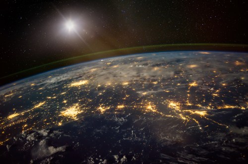 A view of Earth from space, showcasing city lights at night under a starry sky with a bright sun in the background.