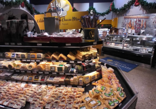 A display of various cheeses in a grocery store, with festive decorations in the background.