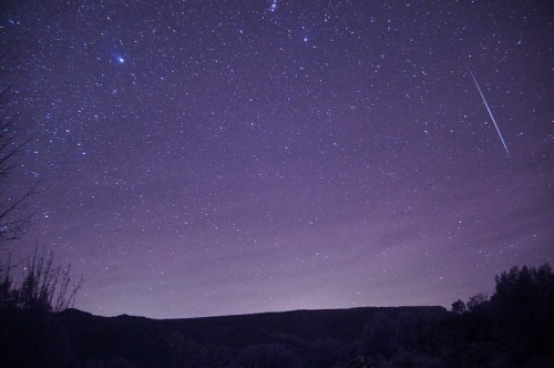 A starry night sky filled with twinkling stars and a faint meteor streaking across the horizon.