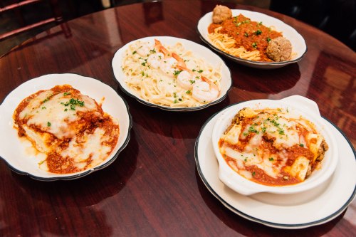 Four plates of Italian pasta dishes, including lasagna, fettuccine with shrimp, spaghetti with meatballs, and baked pasta.