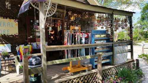 A quaint general store with colorful merchandise displayed on a porch surrounded by greenery and flowers.