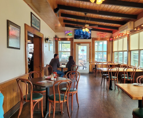 Cozy restaurant interior with wooden decor, tables, and a couple sitting at a table, watching a TV.