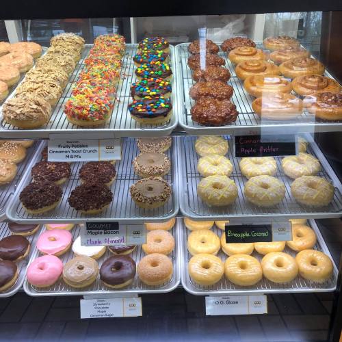 A display case filled with various colorful donuts, including glazed, frosted, and specialty varieties.