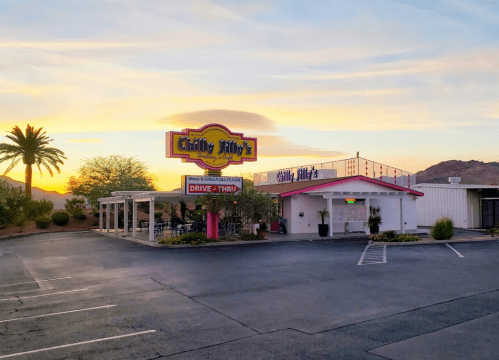 A colorful restaurant sign at sunset, with palm trees and a spacious parking lot in the foreground.