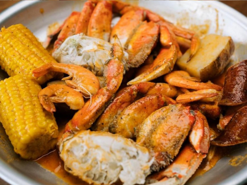 A platter of seafood featuring shrimp, crabs, corn on the cob, and potatoes, all seasoned and cooked together.