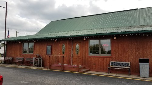 A wooden building with a green metal roof, featuring two front doors and an "OPEN" sign in the window.