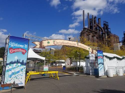 Entrance to Christkindlmarkt Bethlehem with festive signage and industrial buildings in the background.