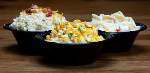 Three bowls of side dishes: one with creamy corn, one with pasta salad, and one with a chicken and bacon mix.