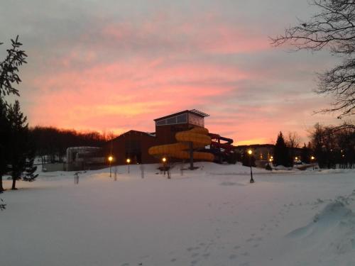 A snowy landscape at sunset, featuring a water slide structure and trees silhouetted against a colorful sky.