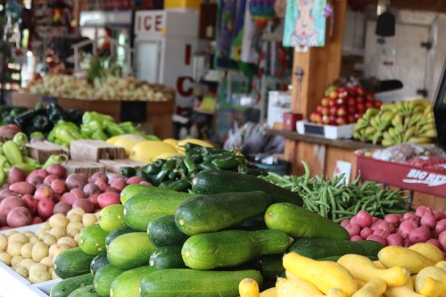 A vibrant display of fresh vegetables and fruits at a market, including zucchinis, potatoes, and bananas.