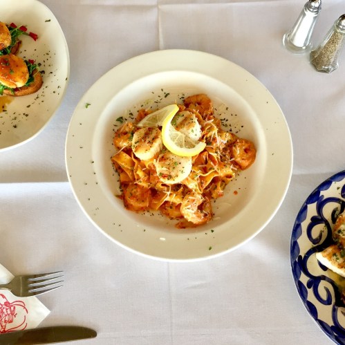 A plate of pasta with a creamy sauce, garnished with lemon and herbs, alongside two other dishes on a white tablecloth.
