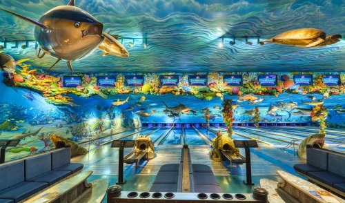 A vibrant bowling alley with ocean-themed decor, featuring large fish and turtles on the walls and ceiling.