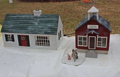 A miniature house and school, both with festive decorations, displayed on a white tablecloth outdoors.