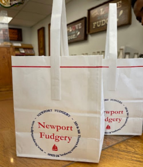 White paper bags with red accents, featuring the logo and name "Newport Fudgery" on a wooden table.