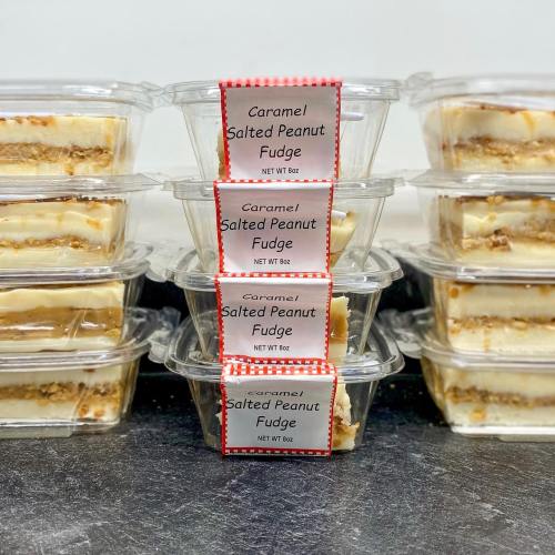 Containers of caramel salted peanut fudge stacked on a countertop, labeled with their contents and weight.