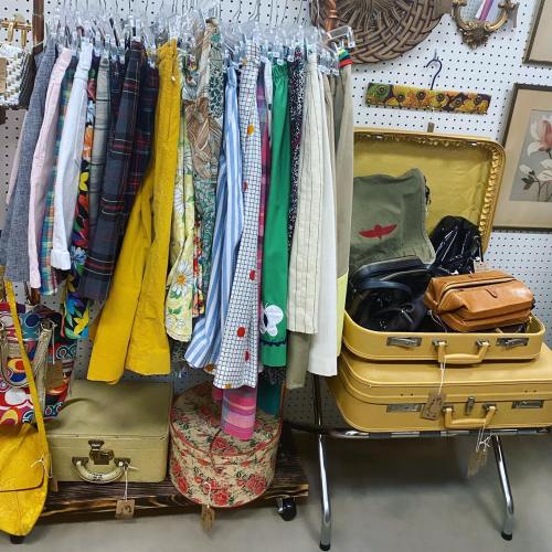 A colorful display of vintage clothing and accessories, including suitcases and bags, on a pegboard backdrop.